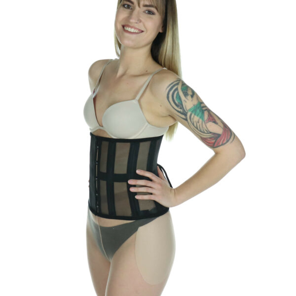 Quartering view of model wearing mesh waist trainer smiling with hand on waist, and wearing Sculptress silicone hip pads